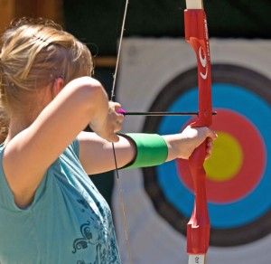 Young girl with target in the background, pulling back an arrow through her bow