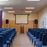 blue chairs in a function room with screen and lecturn at the front