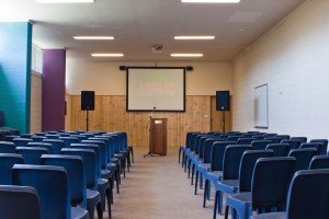 blue chairs in a function room with screen and lecturn at the front