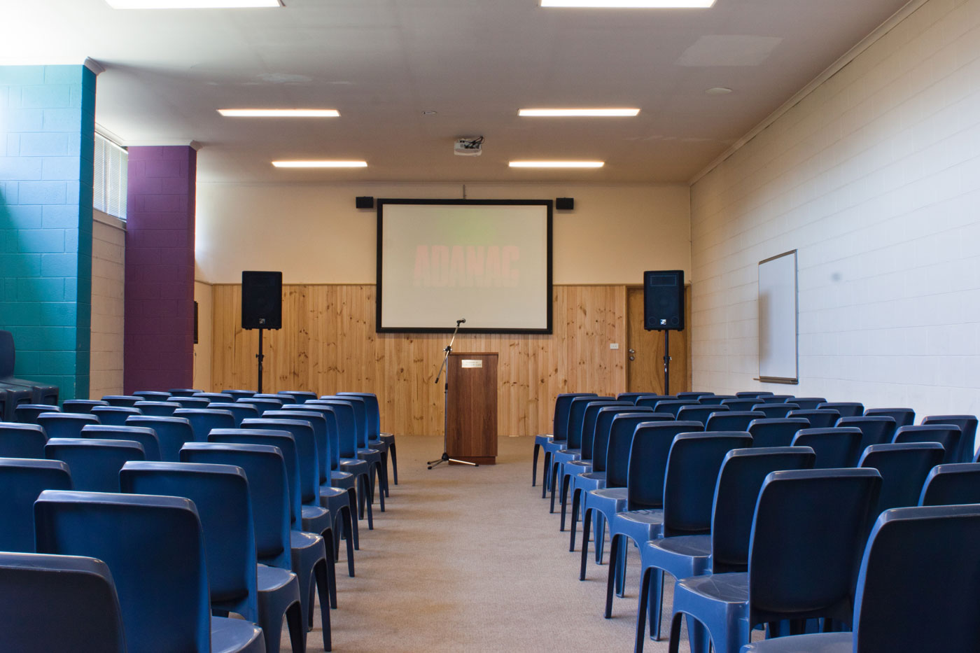 blue chairs in a function room with screen and lecturn at the front